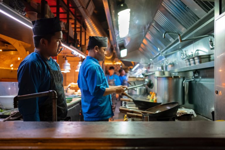 Kitchen Staff Cookig Over Commercial Canopy